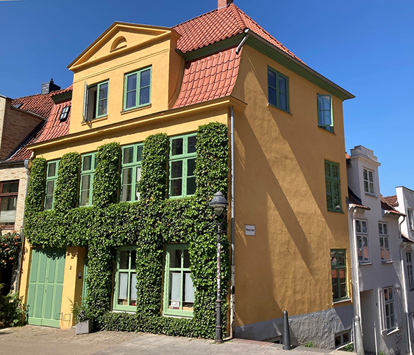 Denkmalgeschütztes Haus nach der Sanierung: ockergelbe Fassade, grüne Sprossenfenster und Efeu